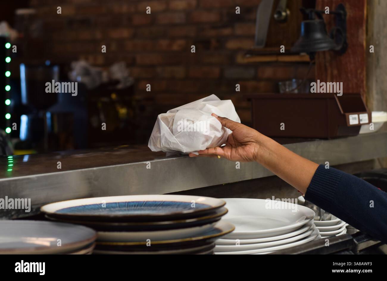 Le mani di una dipendente della tavola calda preparano il panino confezionato per il prelievo Foto Stock