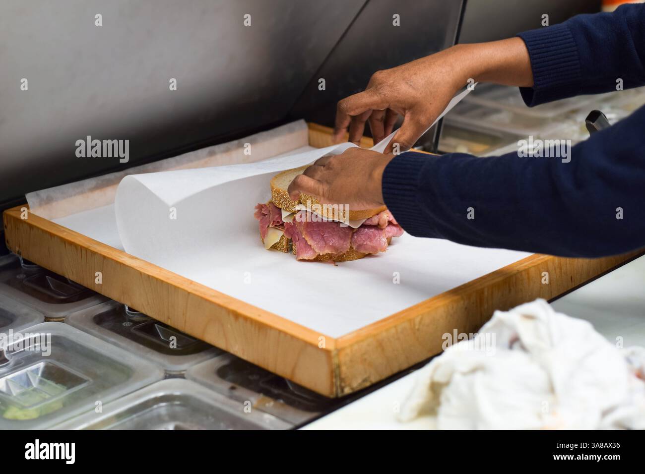 Il dipendente del ristorante Hands of Woman confeziona sandwich di carne di manzo in scatola per l'ordine di asporto in carta cera Foto Stock