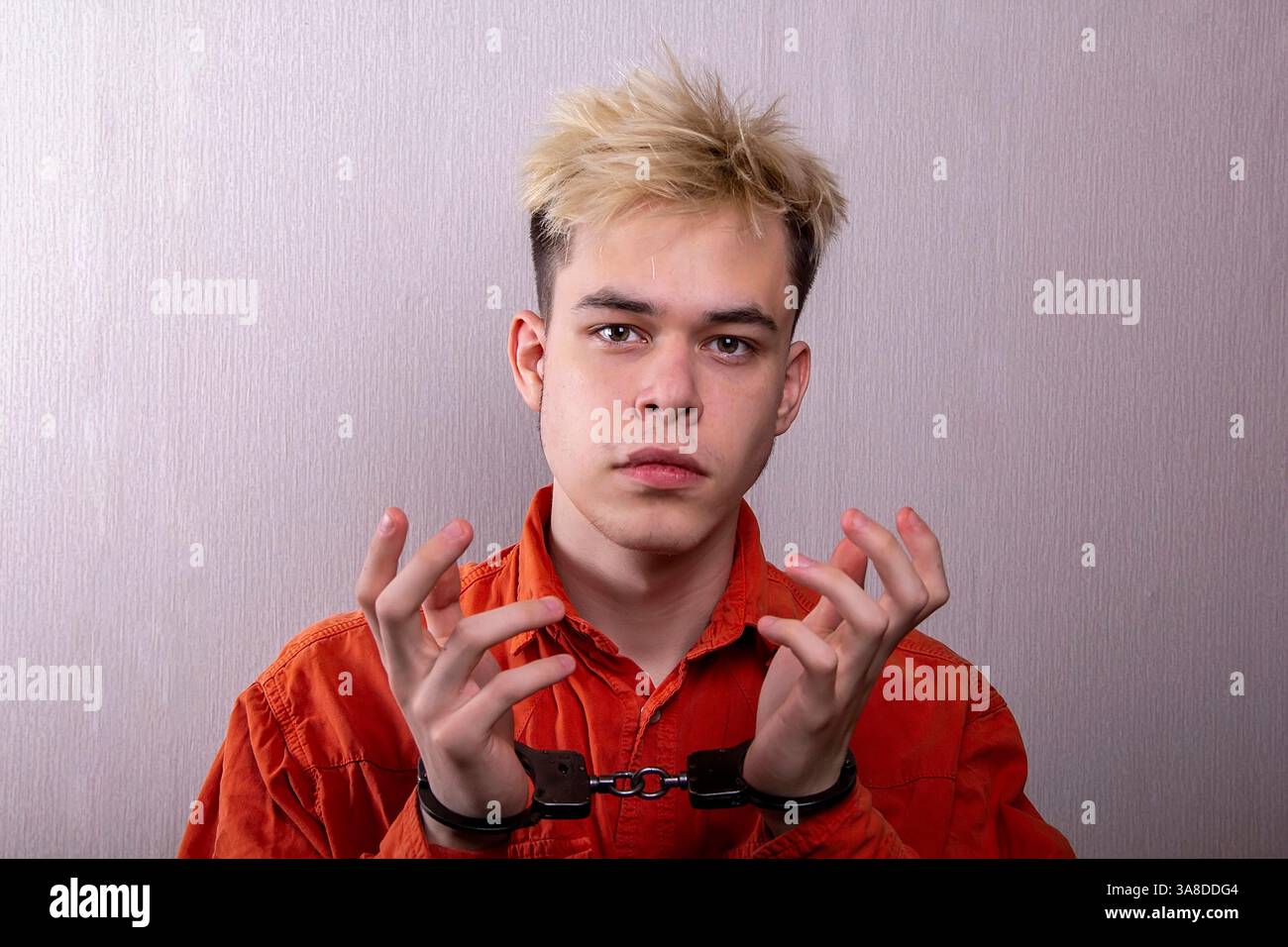 Un giovane uomo in una veste da prigione arancione con le manette sulle mani Foto Stock