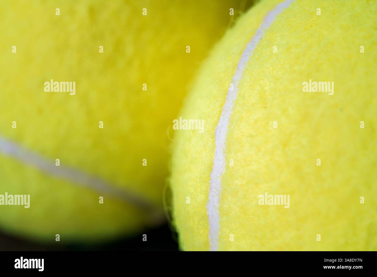 Primo piano di una palla da tennis gialla brillante con una texture sfocata e una linea curva bianca, perfetta per lo sport e i design legati al fitness. Foto Stock