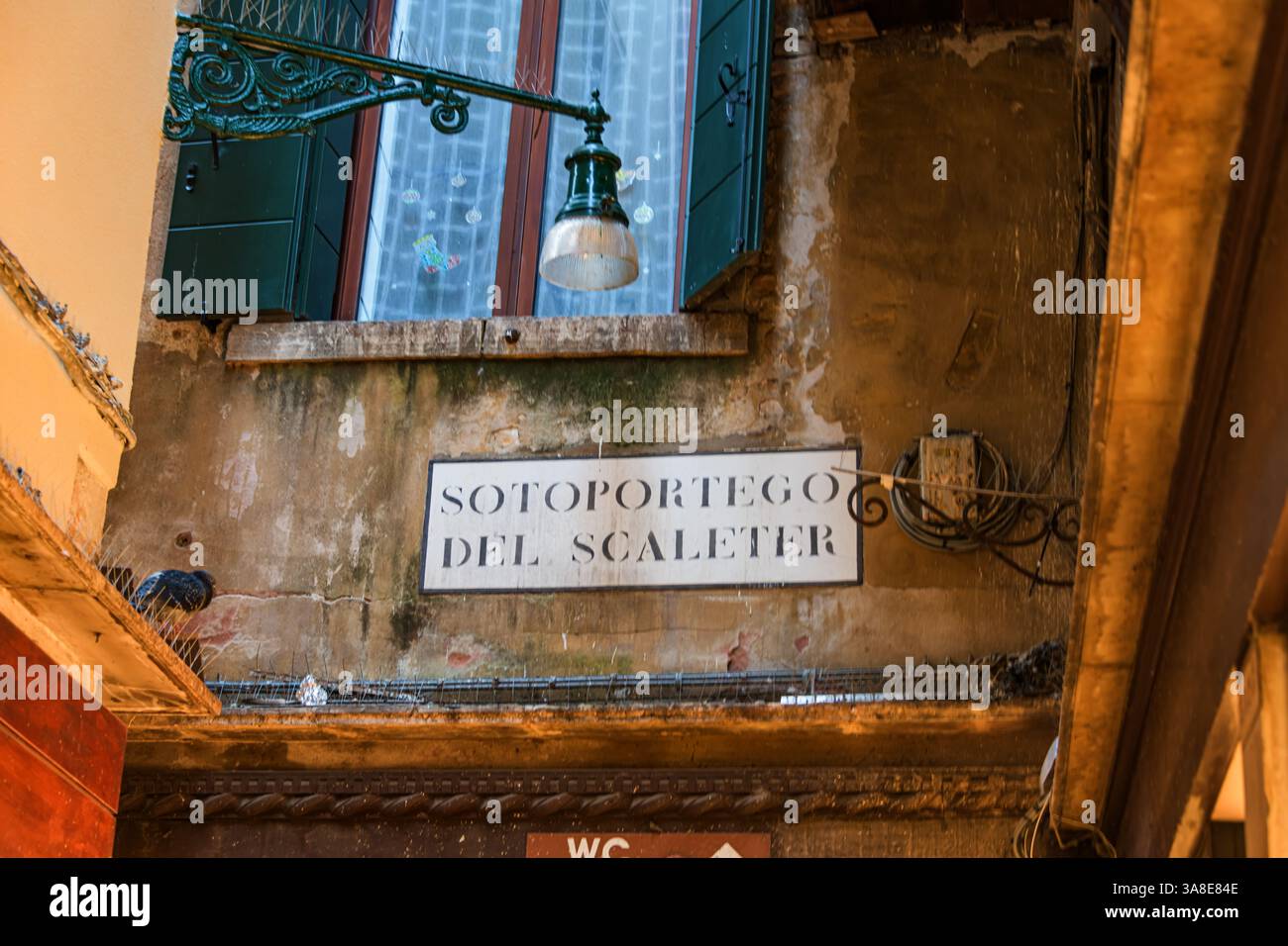 Tradizionale finestra veneziana con persiane verdi e cartello stradale "Sotoportego del Scaleter" in un vicolo storico, Venezia, Italia Foto Stock