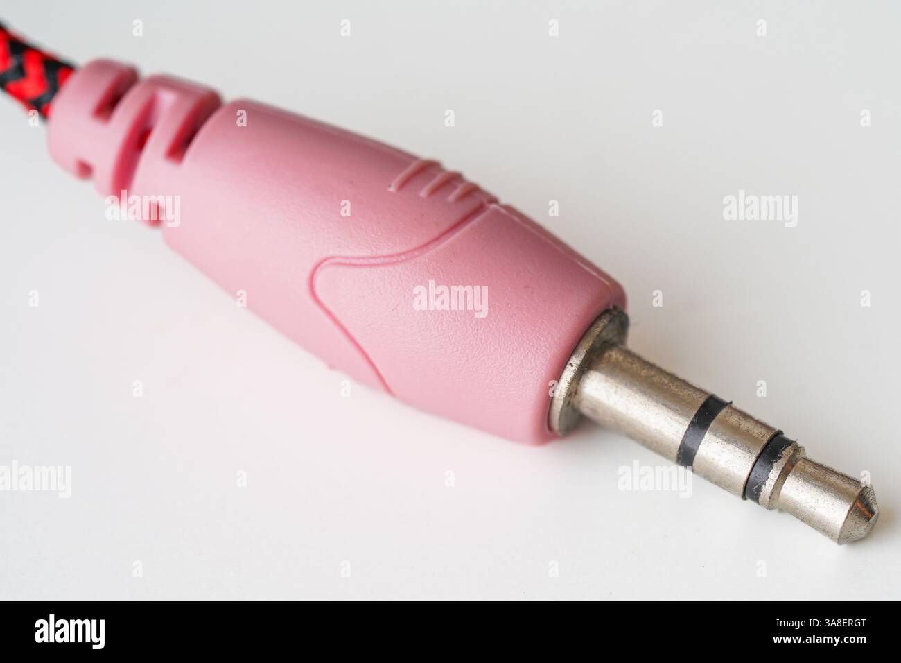 Primo piano di un jack audio rosa da 3,5 mm su sfondo bianco, con spina in metallo e involucro in plastica per i collegamenti audio. Foto Stock