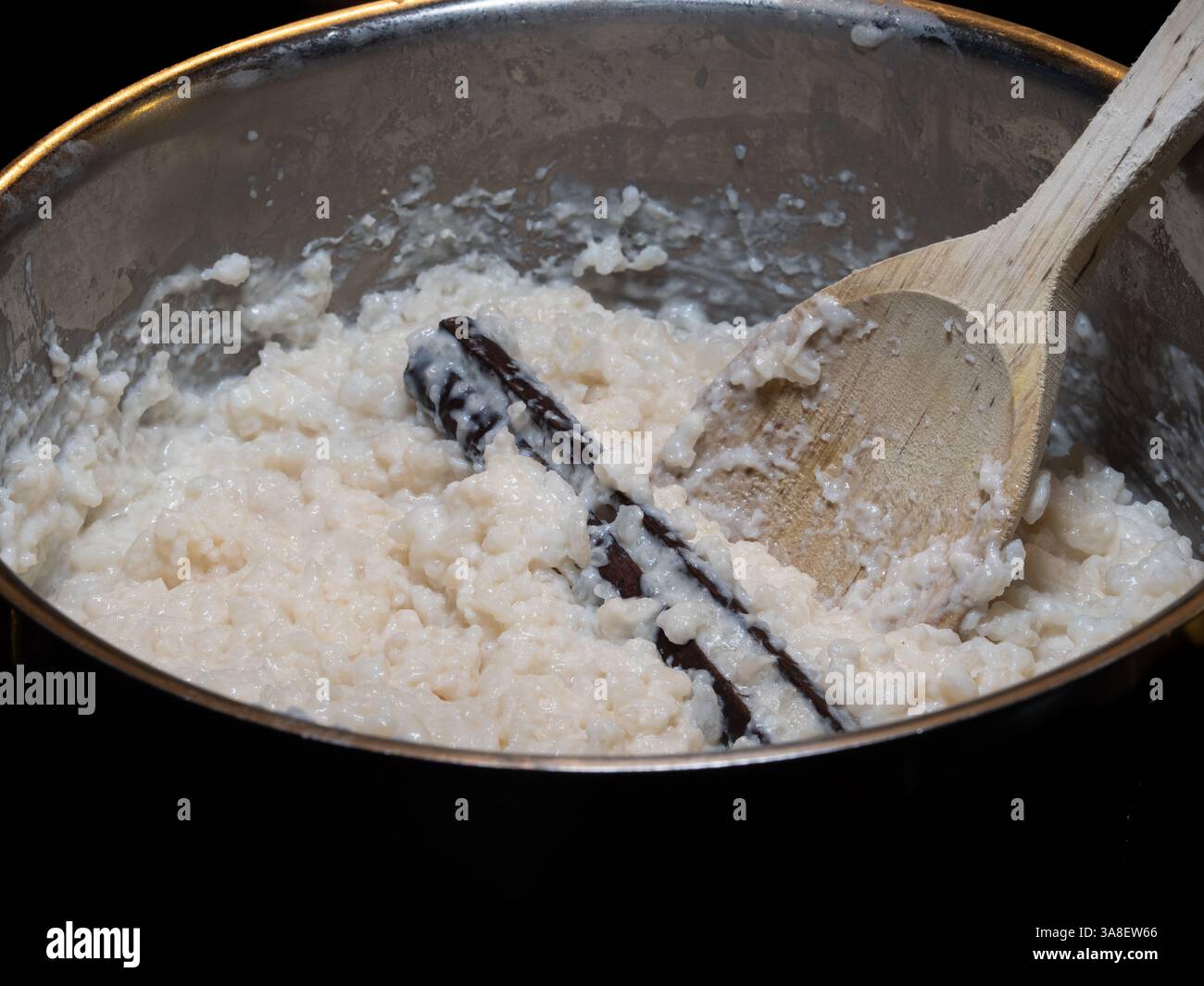 Una scena calda e invitante di un classico budino di riso svedese, ricco e cremoso, servito con un bastoncino di cannella in una pentola, accompagnato da un cucchiaio di legno, set Foto Stock