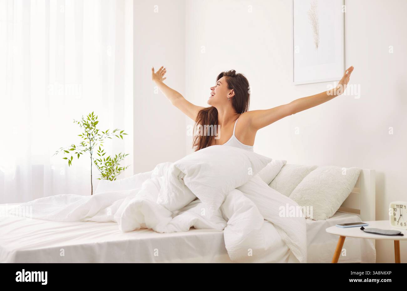 Donna felice che si sveglia e si allena nel letto mentre guarda fuori dalla finestra Foto Stock