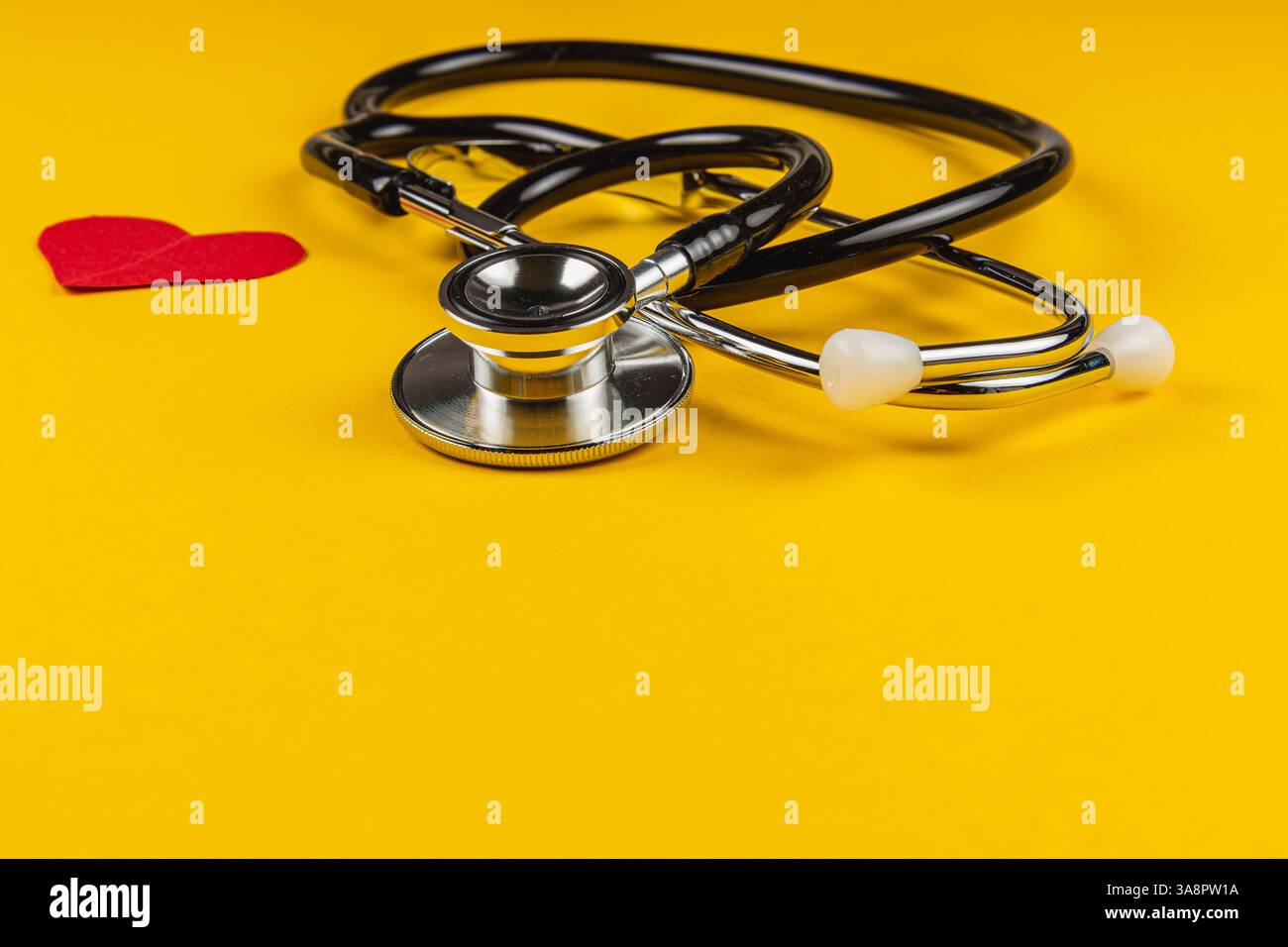 Uno stetoscopio è posizionato accanto a una forma di cuore rosso su un vibrante sfondo giallo, simboleggiando le professioni sanitarie, sanitarie e mediche in una semplice Foto Stock