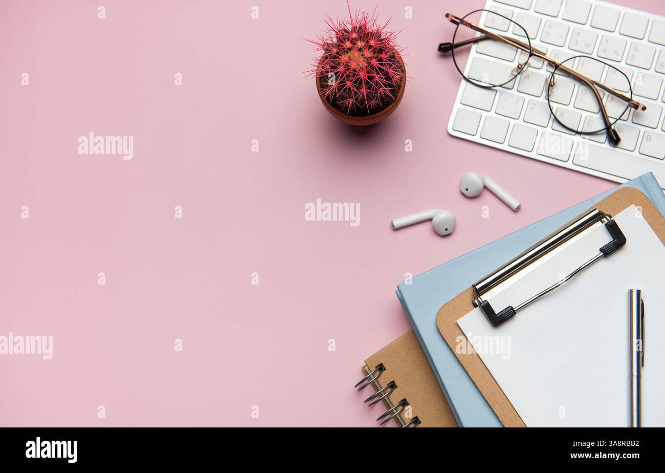 Forniture per ufficio e dispositivi tecnologici disposti in modo ordinato su un desktop rosa, creando uno spazio di lavoro ideale per la produttività e la concentrazione Foto Stock