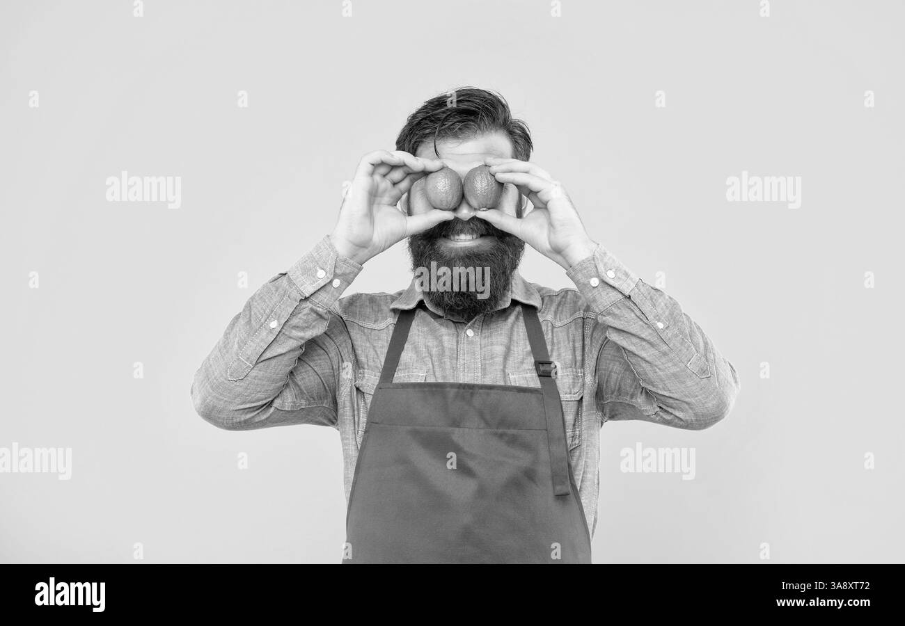 Ragazzo felice in grembiule che tiene lime fresche sugli occhi sfondo giallo, venditore di frutta Foto Stock