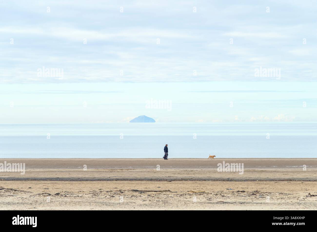 Persone che camminano con un cane a Troon South Beach con Ailsa Craig sullo sfondo, South Ayrshire, Scozia, Regno Unito, Europa Foto Stock