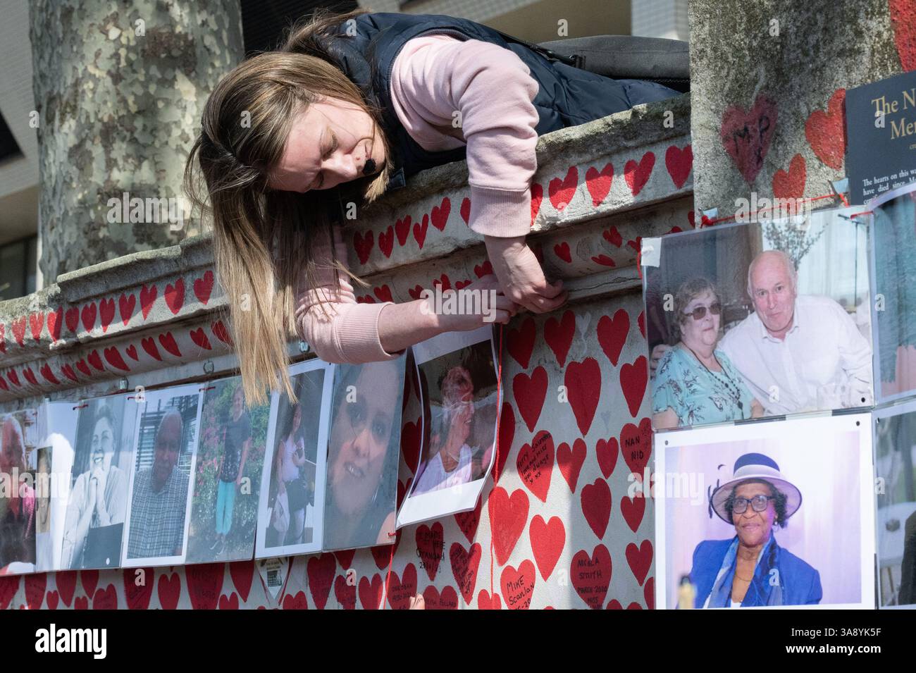 Londra, Regno Unito. 29 marzo 2025. Le famiglie e i parenti in lutto celebrano il quarto anniversario della creazione del National Covid Memorial Wall sull'Albert Embankment, proprio dall'altra parte del fiume rispetto al Parlamento. Il tributo non ufficiale si estende per 500 metri con un cuore rosso dipinto a mano raffigurante ciascuna delle oltre 240.000 vittime della pandemia di coronavirus nel Regno Unito. Centinaia di fotografie del defunto pendono lungo il muro che la processione commemorativa percorreva, leggendo tributi lungo il percorso. Crediti: Ron Fassbender/Alamy Live News Foto Stock