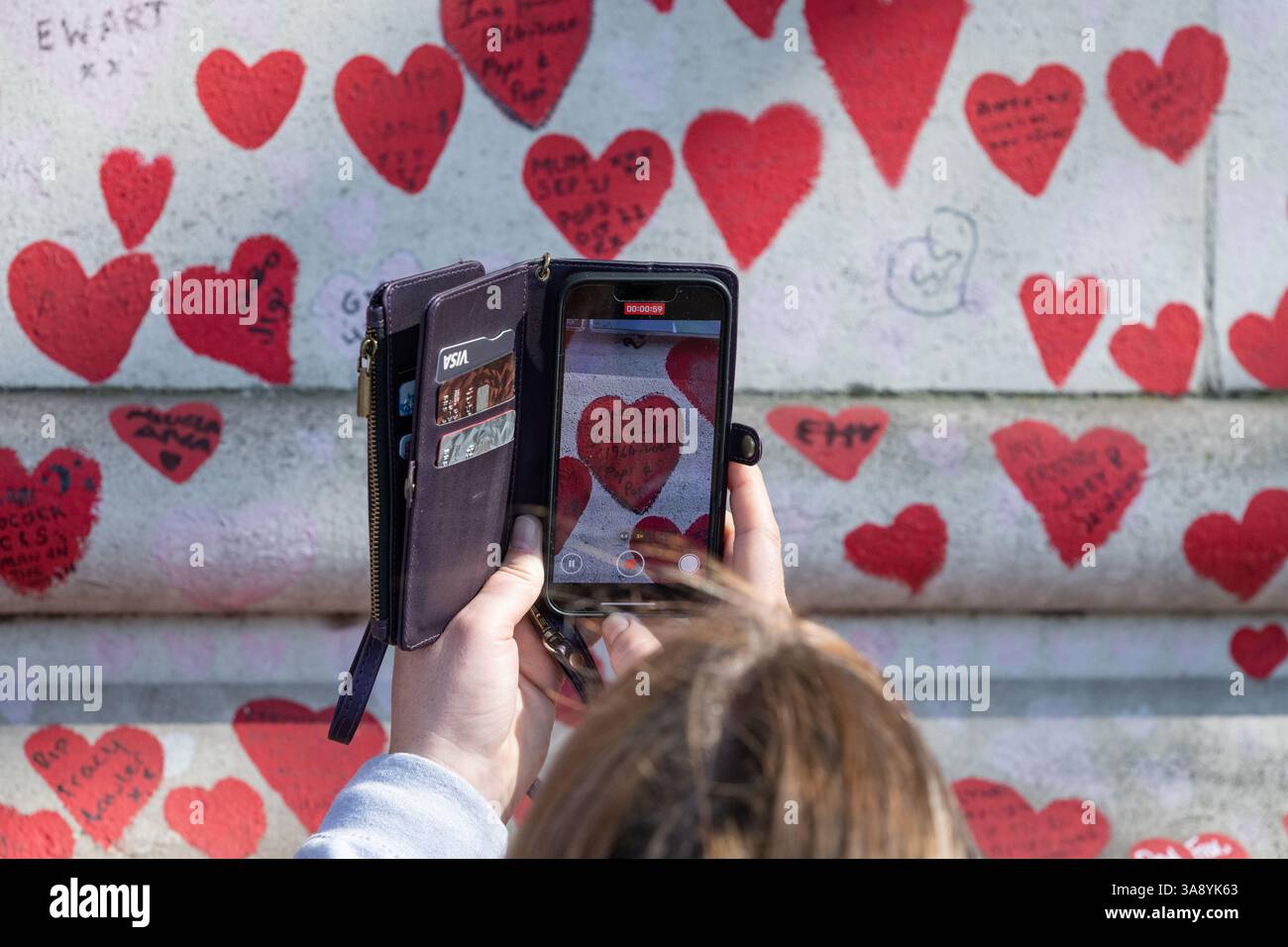 Londra, Regno Unito. 29 marzo 2025. Le famiglie e i parenti in lutto celebrano il quarto anniversario della creazione del National Covid Memorial Wall sull'Albert Embankment, proprio dall'altra parte del fiume rispetto al Parlamento. Il tributo non ufficiale si estende per 500 metri con un cuore rosso dipinto a mano raffigurante ciascuna delle oltre 240.000 vittime della pandemia di coronavirus nel Regno Unito. Centinaia di fotografie del defunto pendono lungo il muro che la processione commemorativa percorreva, leggendo tributi lungo il percorso. Crediti: Ron Fassbender/Alamy Live News Foto Stock