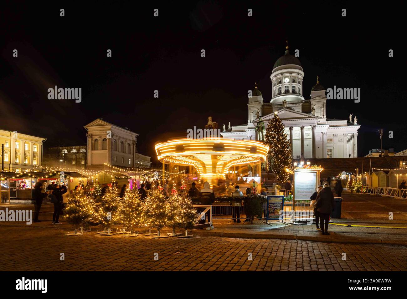 Movimento sfocato di una giostra con la Cattedrale di Helsinki illuminata sullo sfondo. Mercatino di Natale di Helsinki dopo il tramonto in Piazza del Senato, Helsinki. Foto Stock