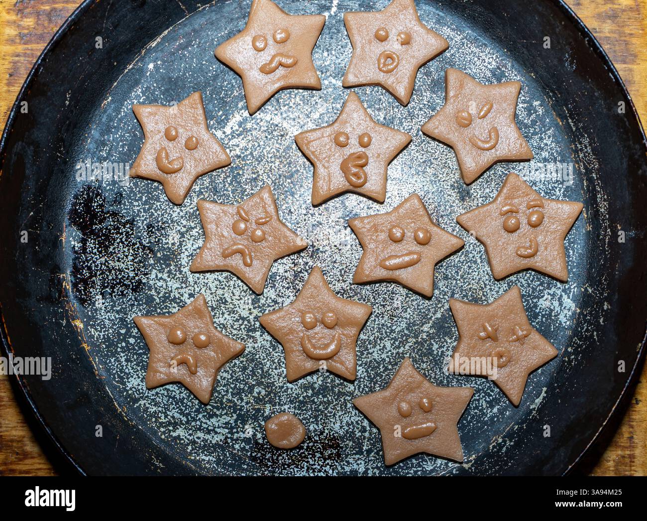 Un vassoio contiene biscotti appena preparati a forma di stella, ognuno con espressioni facciali uniche. I biscotti sono fatti con l'impasto e sono pronti per la cottura Foto Stock