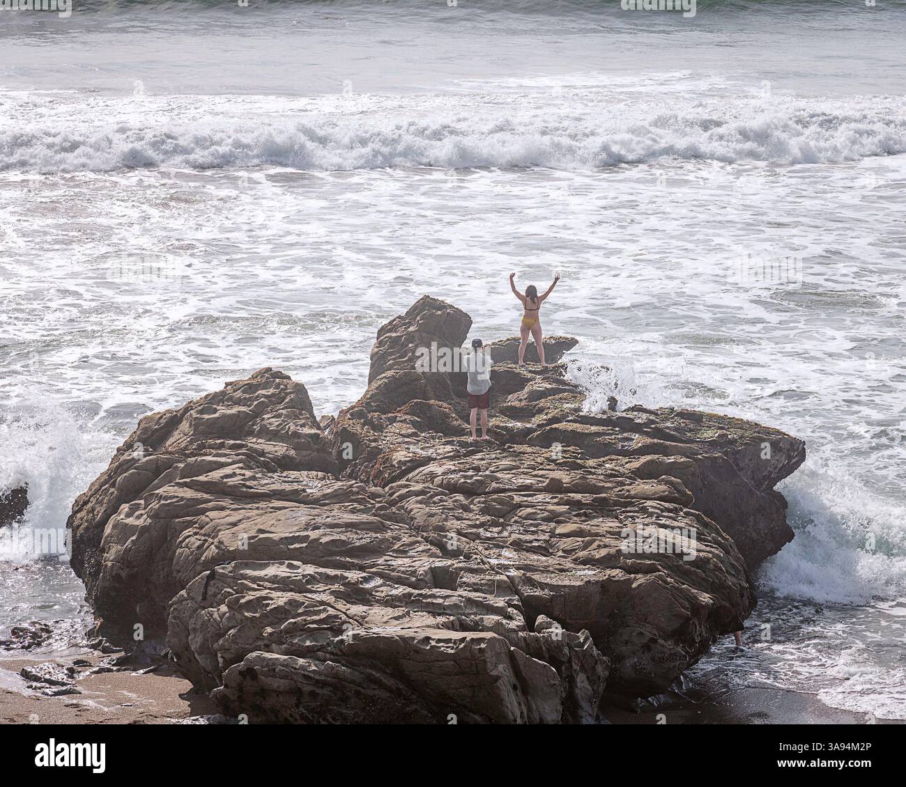 Cambria, CA, USA: 27 marzo 2025: I visitatori si trovano su una roccia a Moonstone Beach a Cambria, CA. Foto Stock