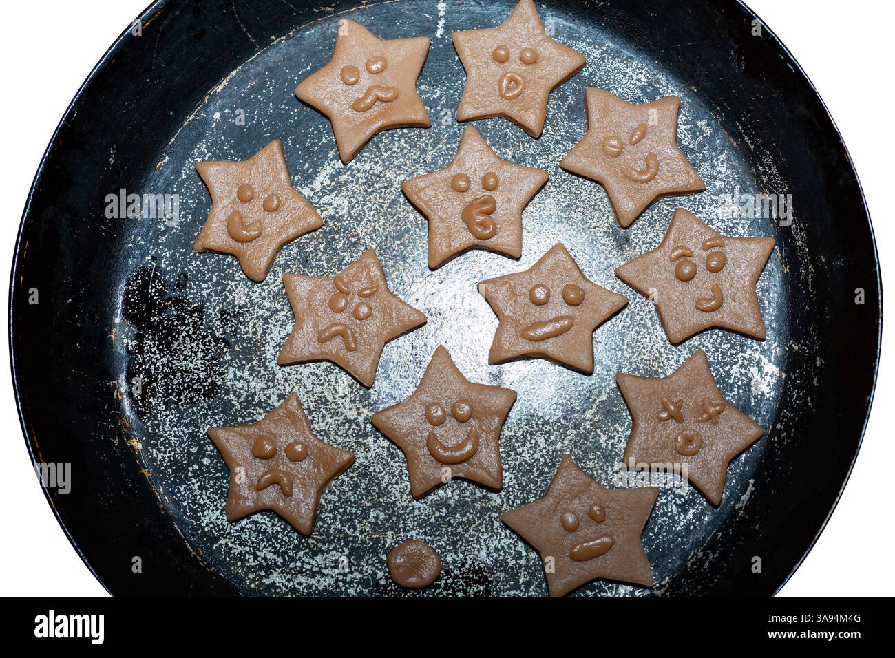 Deliziosi biscotti a forma di stella di cioccolato sono disposti in una teglia rotonda, ciascuno decorato con giocose espressioni facciali. Questi dolcetti sono pronti per la cottura di Foto Stock