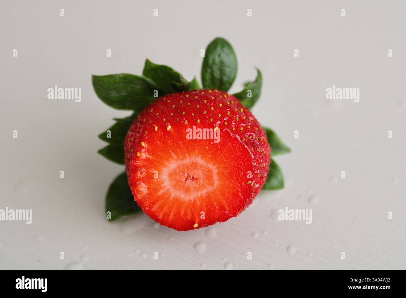 Mezza fragola succosa con gocce d'acqua su sfondo bianco. Fresco, vivace e pulito. Foto Stock