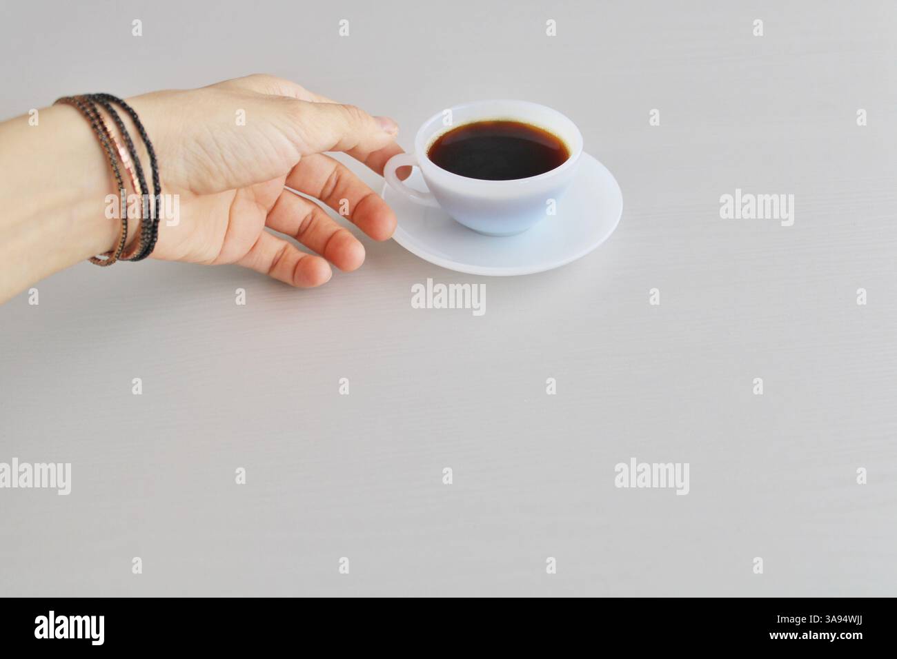 Mano che raggiunge una tazza di caffè nero su una superficie pulita e neutra. Momento mattutino minimo e tranquillo. Foto Stock