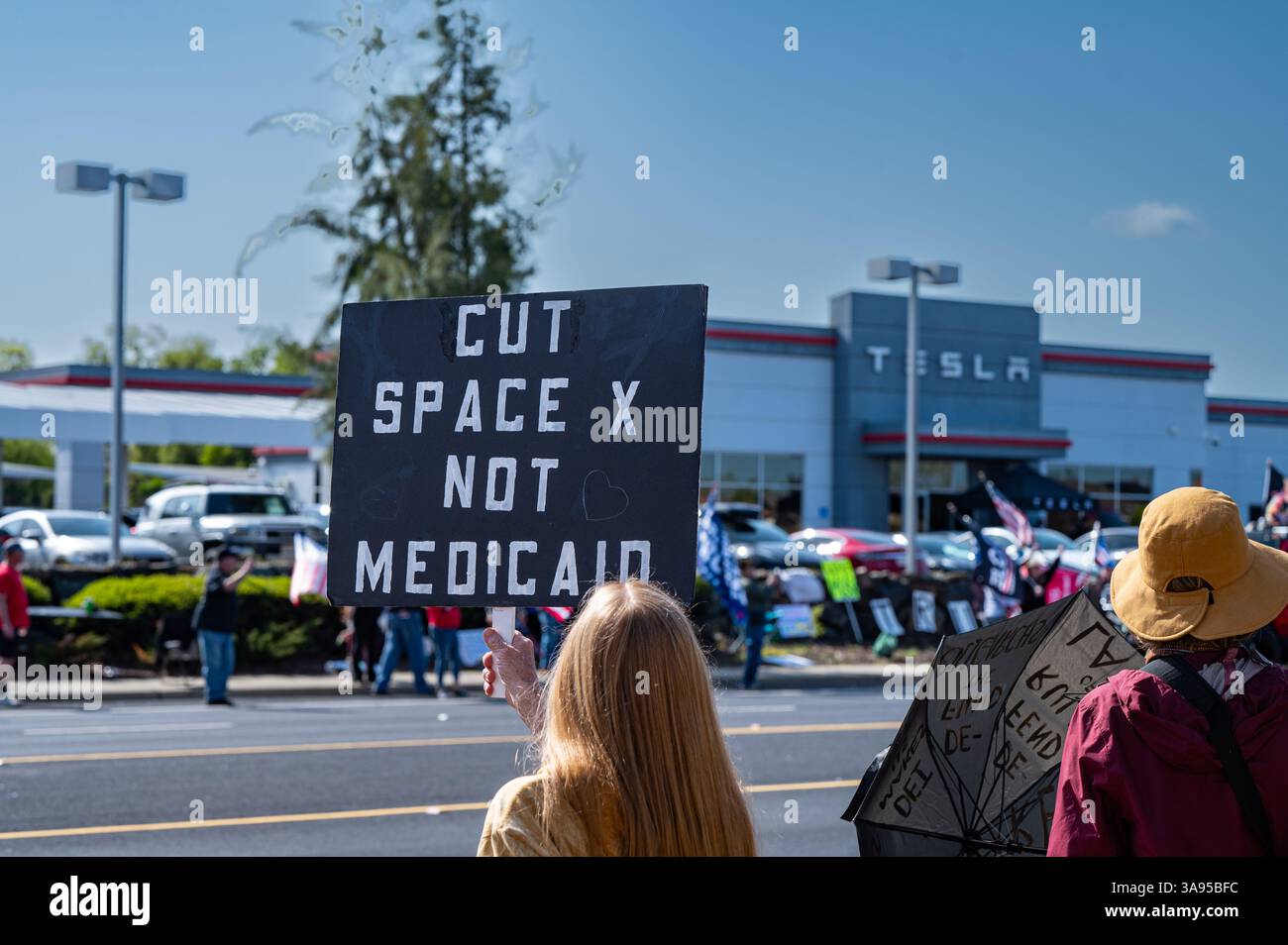 Un manifestante anti-Elon Musk non identificato ha un segnale sul taglio di Space X e non Medicaid di fronte alla concessionaria Tesla e ai manifestanti. Foto Stock