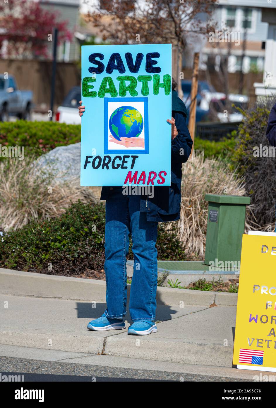 Un protestatore anti-Elon Musk in un raduno della concessionaria Tesla ha un segnale su come salvare il pianeta Terra e dimenticare il pianeta Marte. Foto Stock