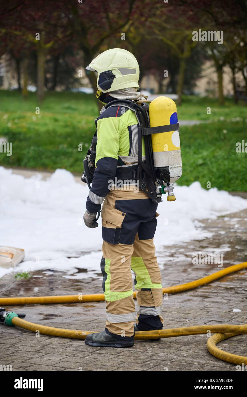 Un vigile del fuoco che indossa indumenti protettivi completi, tra cui un casco, una tuta ignifuga, guanti e un autorespiratore (SCBA), si distingue per Foto Stock