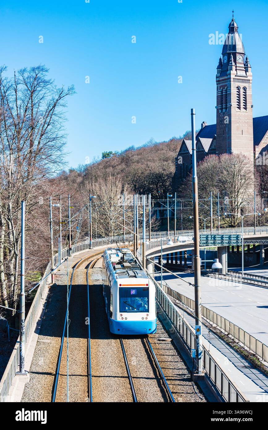 Un tram si sposta lungo i binari di Goteborg, incorniciati da alberi ed edifici storici sotto il cielo azzurro e limpido nel calore della primavera. L'energia vibrante Foto Stock