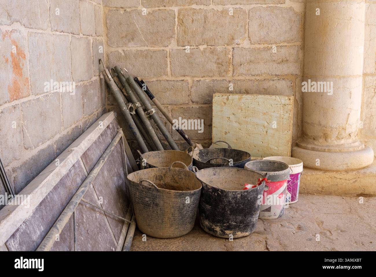 Più secchi, pali per impalcature e superfici piane sono sistemati in modo ordinato in un angolo, indicando gli sforzi di restauro in corso in un edificio storico, Foto Stock