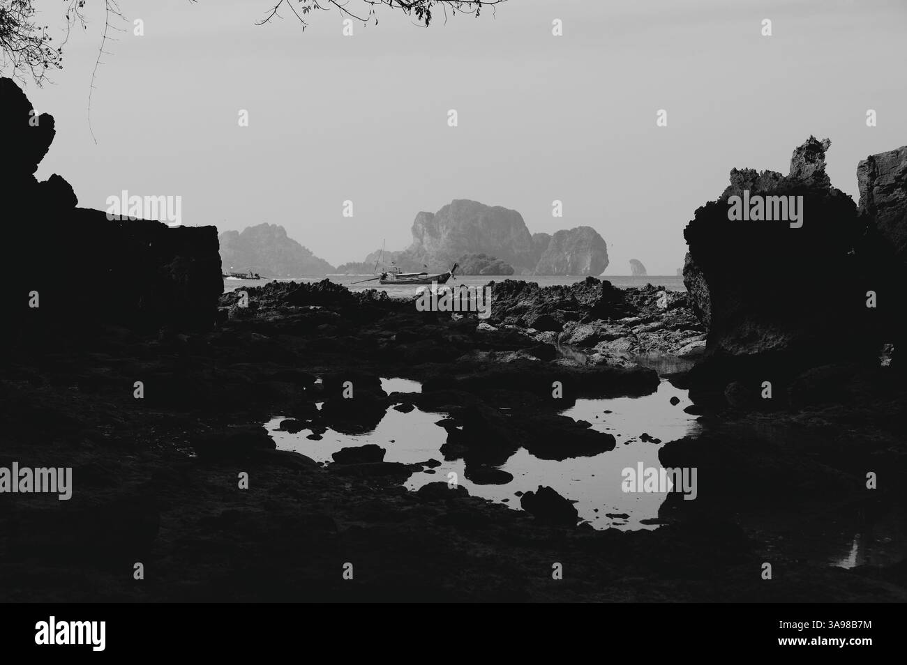 La tradizionale barca tailandese a coda lunga scivola tra le formazioni rocciose frastagliate rivelate dalla bassa marea mattutina Foto Stock