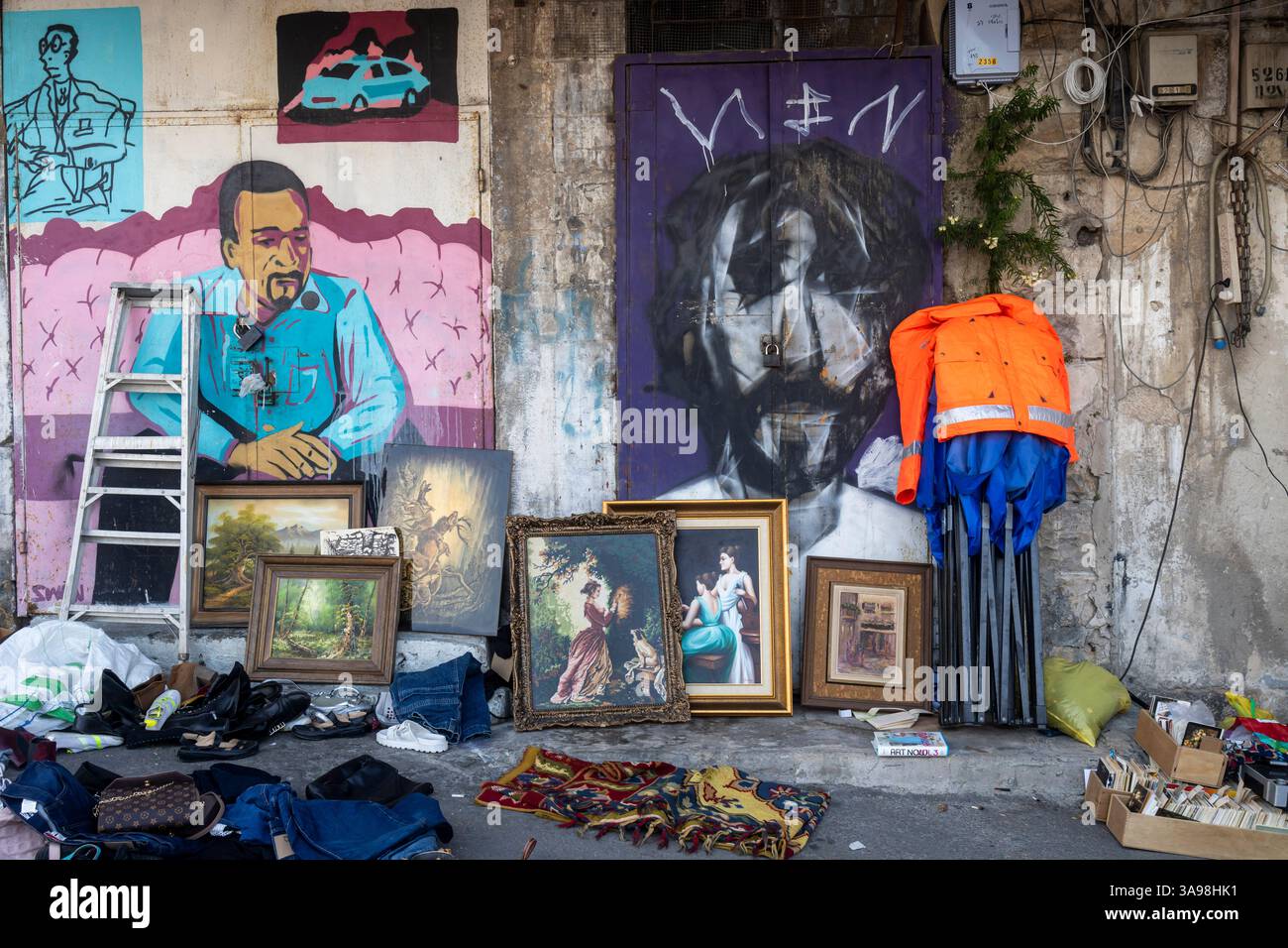 Haifa, Israele, 28 marzo 2025, sotto i dipinti, una pila di vestiti, scarpe e altri oggetti scartati sono sparsi per terra. Un ru con motivo rosso Foto Stock