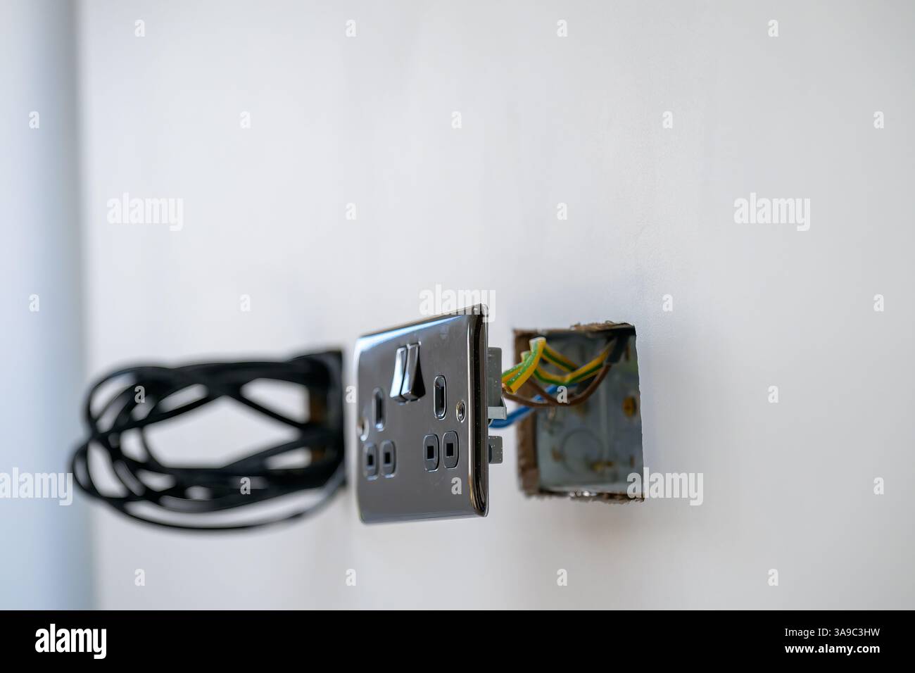 Installazione in corso di una presa elettrica in nichel e di un cablaggio su un impianto elettrico a parete bianca Foto Stock