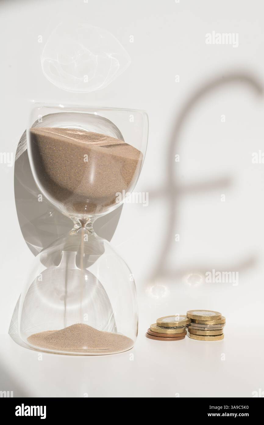 Clessidra con monete e simbolo della sterlina che rappresenta il tempo e il valore finanziario, la sterlina, il limite di tempo in contanti, la valuta Foto Stock