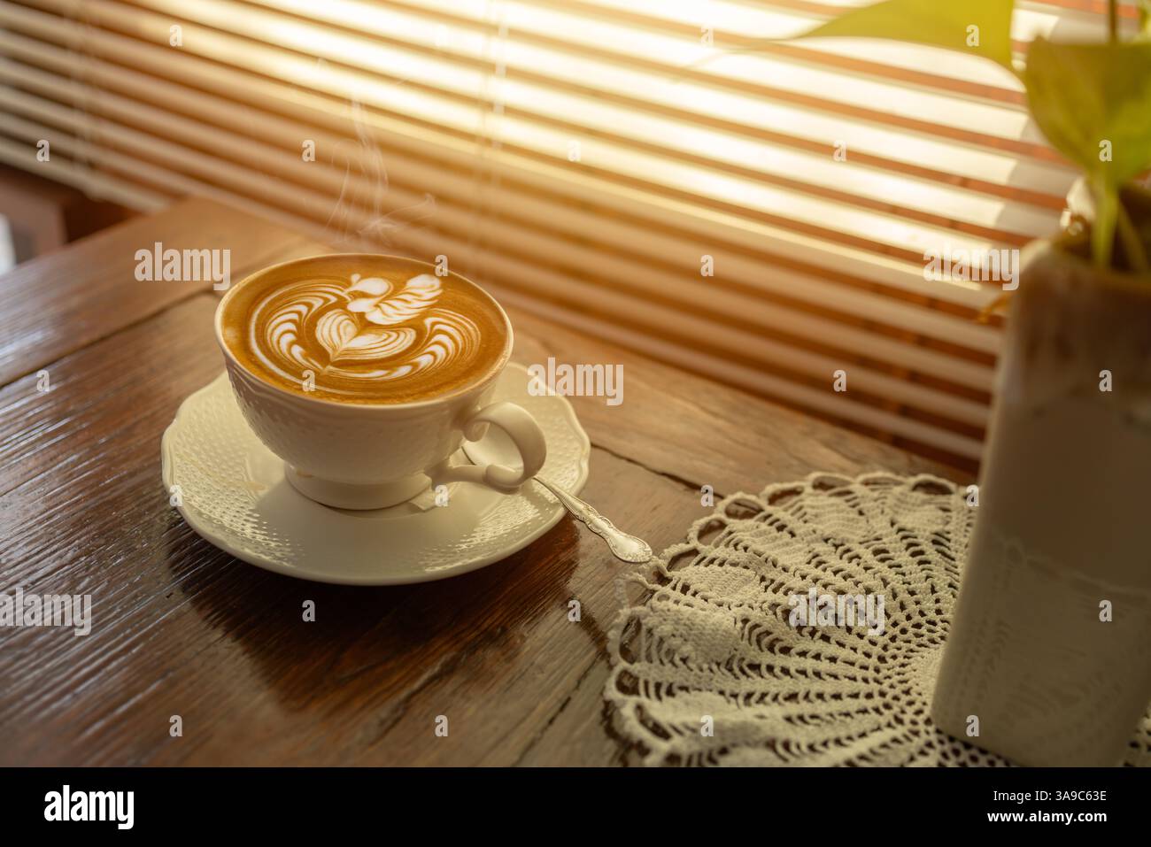 tazza da caffè calda con latte art a lato delle finestre calde con luce solare, ombrellone, bevande rilassanti e accoglienti Foto Stock