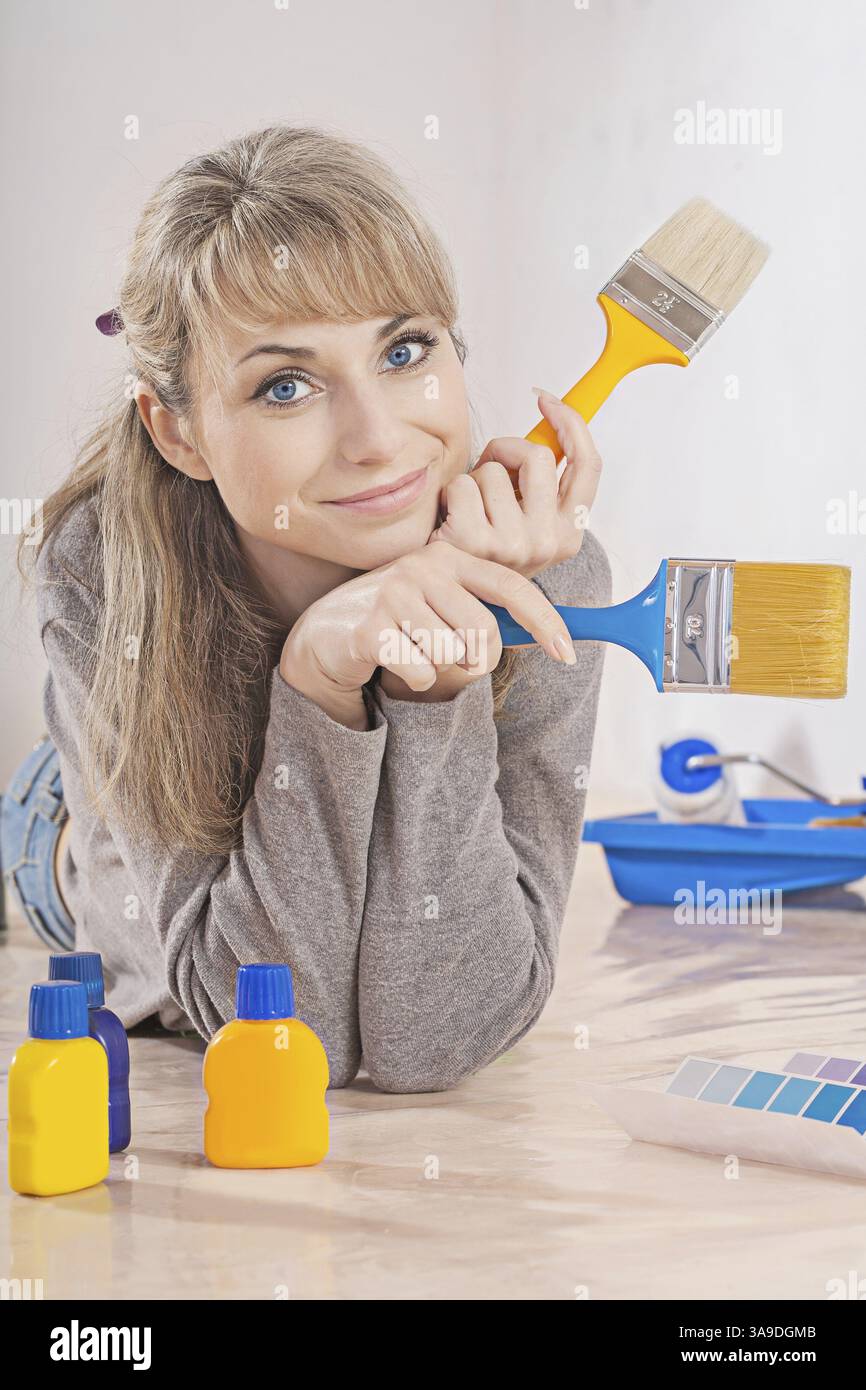 Bella donna sul pavimento con pennelli e altri strumenti che guardano la fotocamera Foto Stock