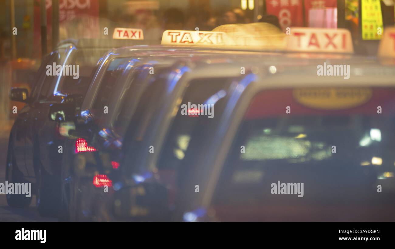Taxi che guidano in fila uno dopo l'altro sulla strada notturna di Hong Kong. Cartelli illuminati sulla parte superiore delle cabine Foto Stock