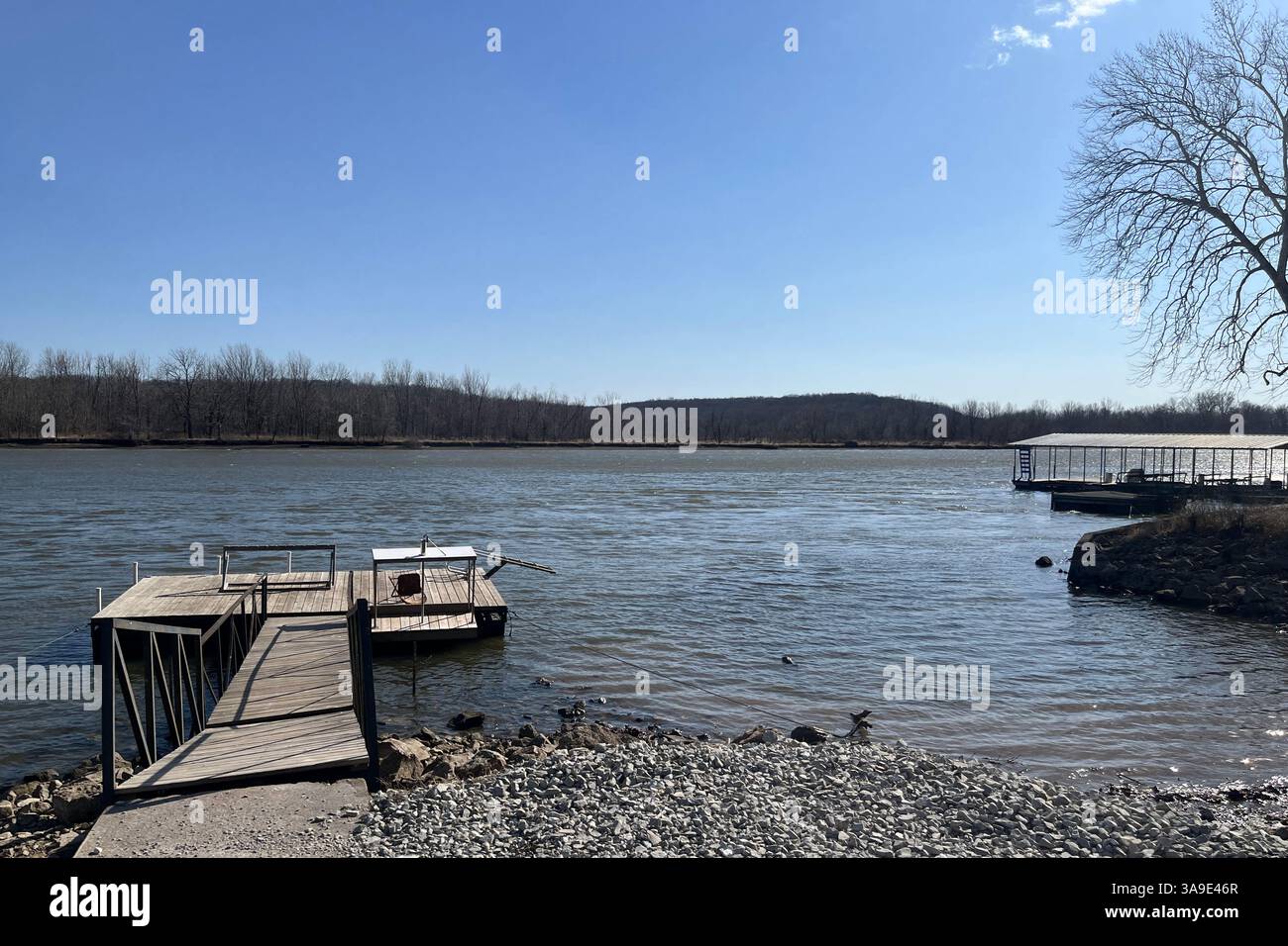 Una tranquilla scena lungo il fiume in una giornata limpida - i moli di legno riposano lungo la costa rocciosa sotto un ampio cielo blu. - Immagine stock catturata con smartphone