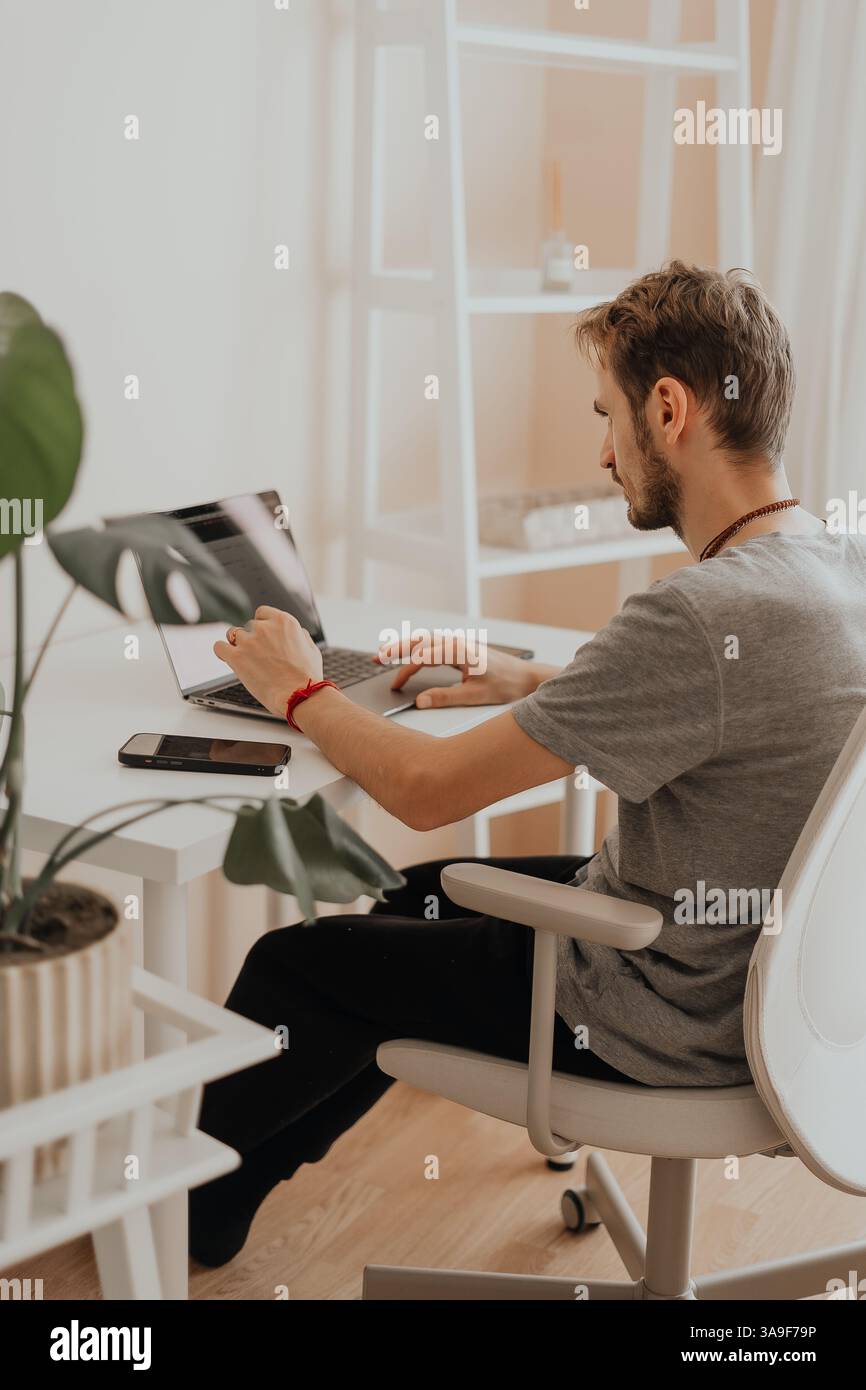 Calma nell'ufficio domestico con le piante. Un uomo lavora in una tranquilla concentrazione a casa, circondato da piante e luce soffusa, con produttività consapevole in azione Foto Stock