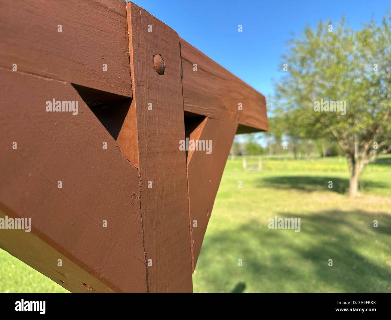 Una robusta trave di legno in un parco illuminato dal sole, che getta ombre su lussureggianti prati verdi e alberi lontani. - Immagine stock catturata con smartphone