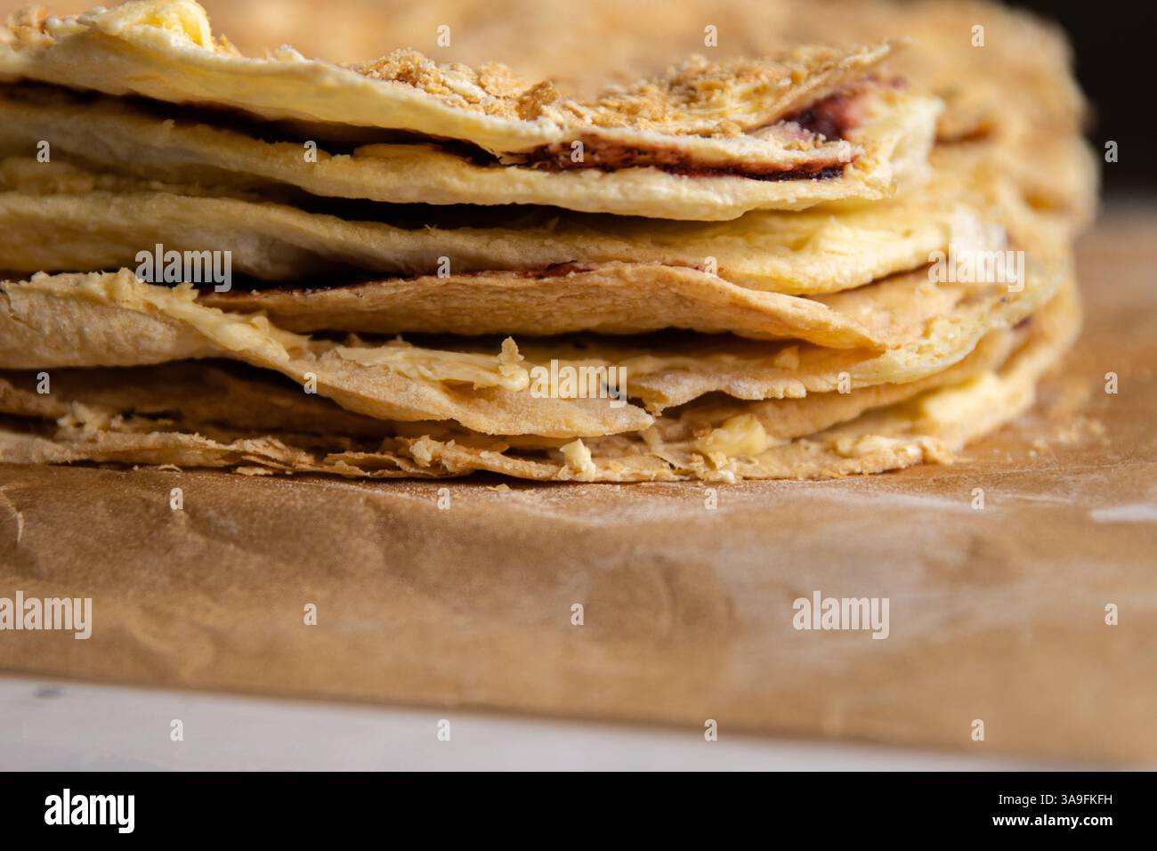 Processo di supporto. Primo piano degli strati di pasta sfoglia della deliziosa torta francese Napoleone stesa sulla carta di supporto. Pasticceria francese con burro crema pasticcera Foto Stock