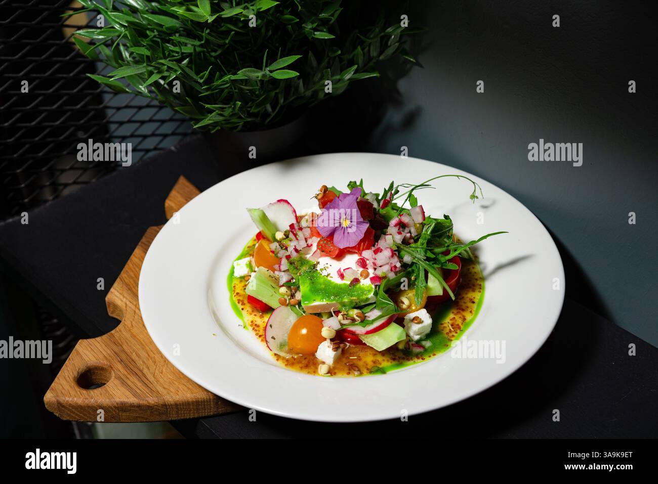 Una vivace insalata gourmet con feta, germogli, cetrioli, ravanello, pomodori ciliegini, e ricoperto di fiori commestibili e condimento. Foto Stock