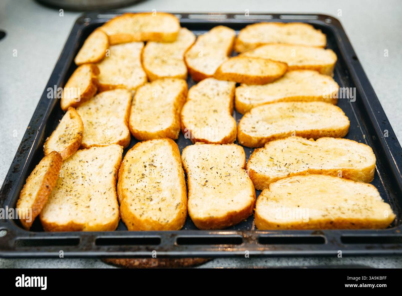 Crostini appena sfornati con erbe aromatiche, disposti ordinatamente su un vassoio da forno scuro per antipasti o contorni. Foto Stock