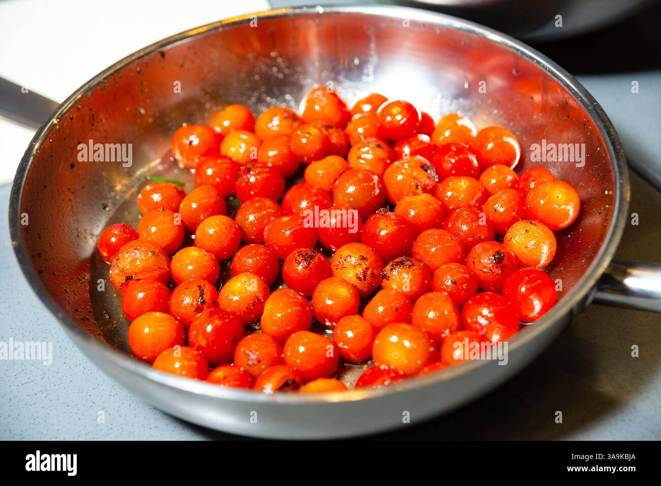 Pomodori ciliegini freschi saltati in padella con olio ed erbe aromatiche, ideali per pasta, insalate o piatti di verdure calde. Foto Stock