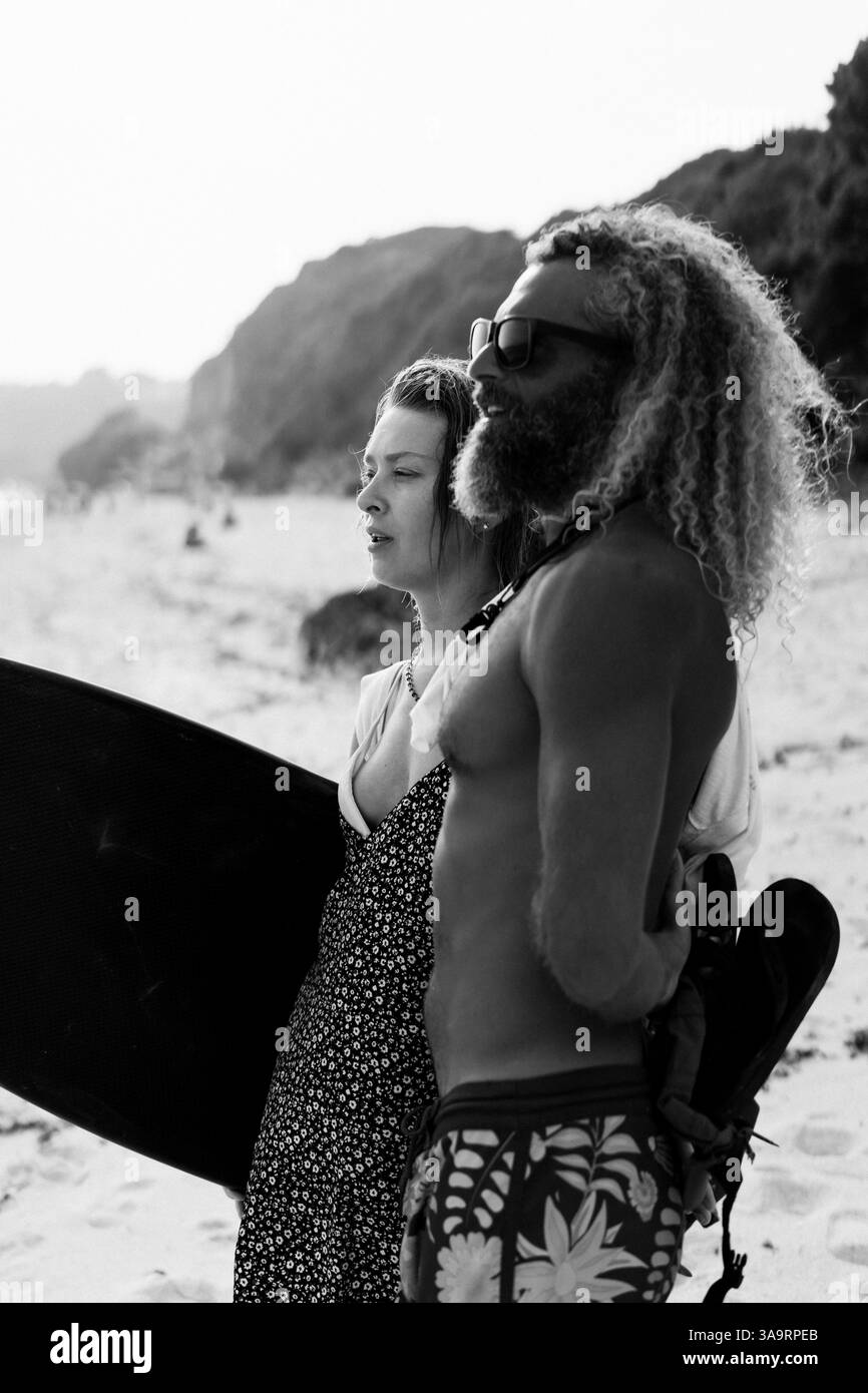 Amici con tavola da surf in piedi in spiaggia Foto Stock
