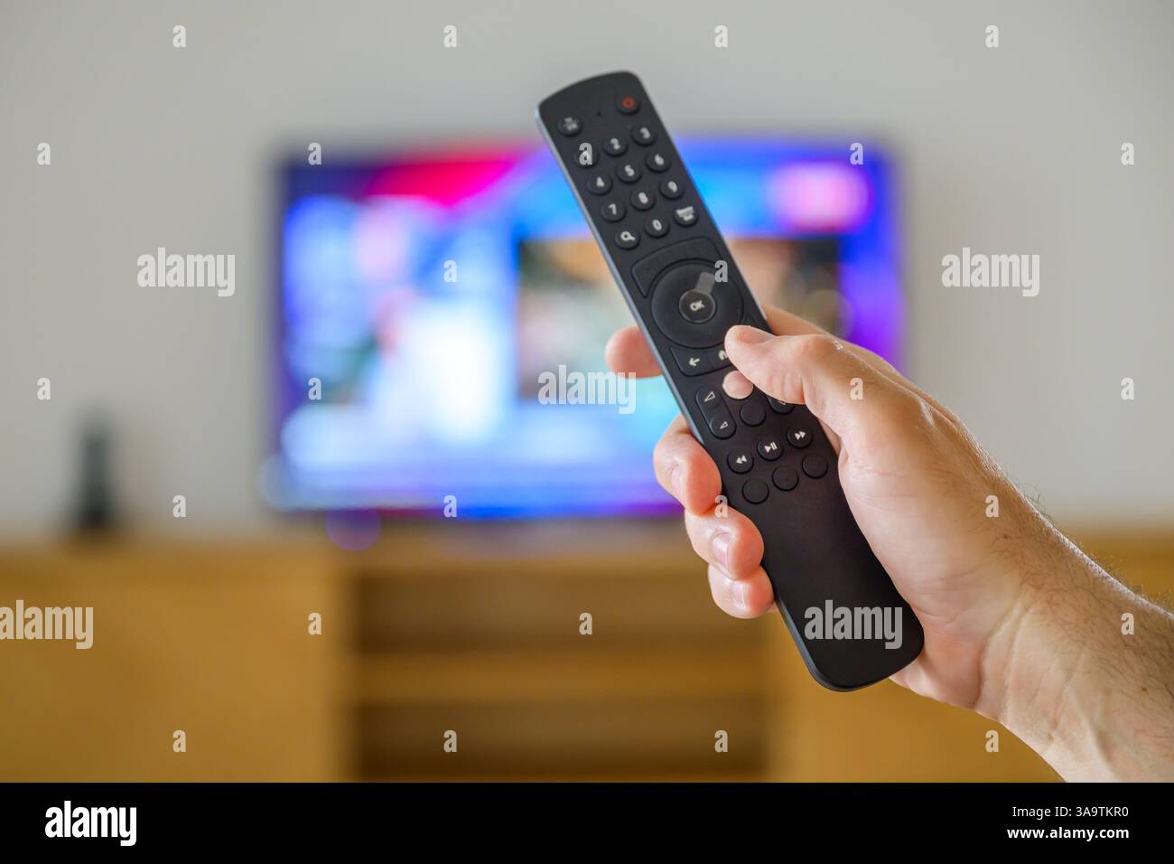 Mano maschile con telecomando TV in soggiorno, messa a fuoco selettiva Foto Stock