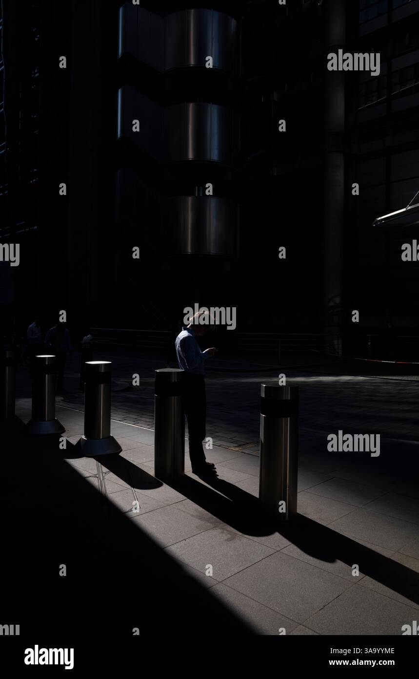 I lavoratori della città si stagliavano per metà alla luce del mattino all'esterno del Lloyds Building in Lime Street, City of London, Inghilterra, Regno Unito Foto Stock