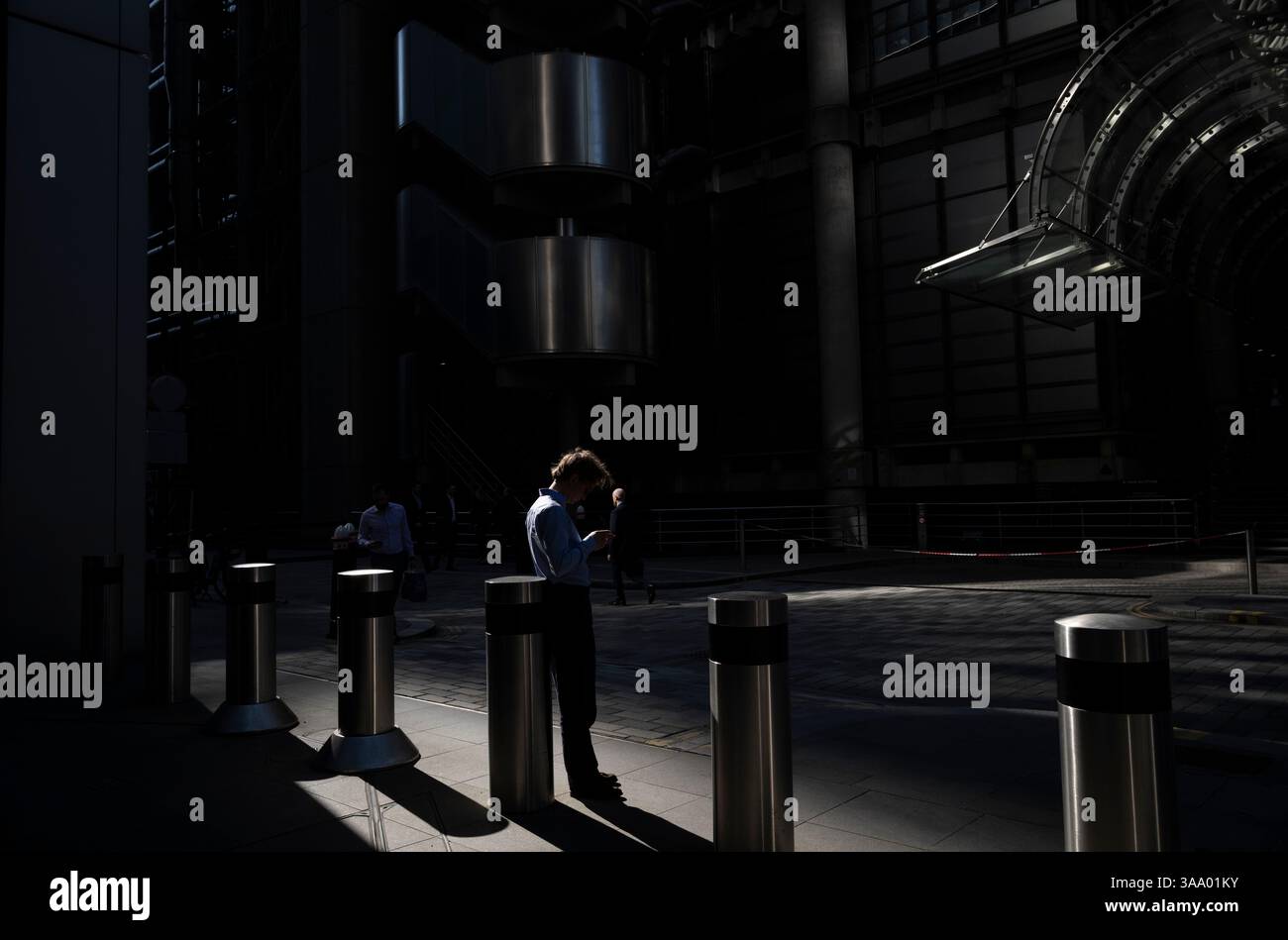I lavoratori della città si stagliavano per metà alla luce del mattino all'esterno del Lloyds Building in Lime Street, City of London, Inghilterra, Regno Unito Foto Stock