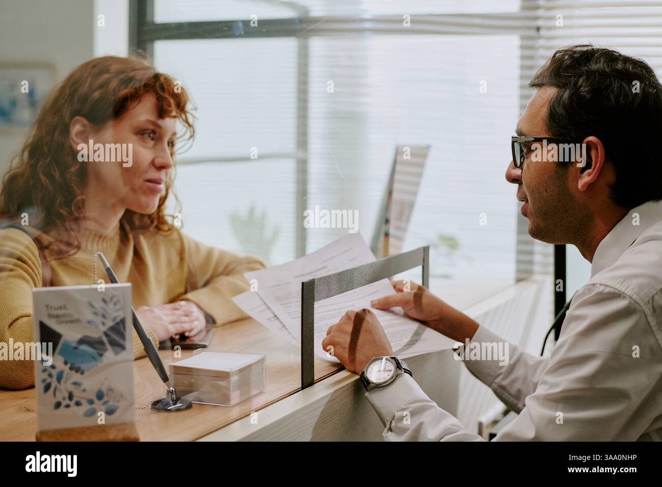 Ambiente di lavoro con due colleghi che discutono documenti all'interno della scrivania, donna con i capelli rossi e uomo con gli occhiali impegnato in conversazione Foto Stock