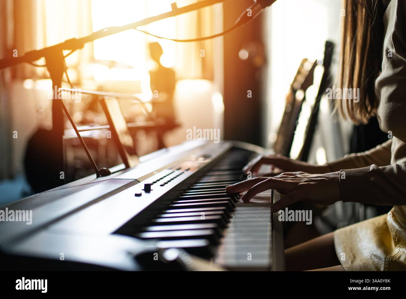 Donna che suona il pianoforte digitale in uno studio musicale illuminato dal sole circondato da chitarre e attrezzature di registrazione, concetto di creatività, produzione musicale, stile di vita e artisti femminili. Foto Stock