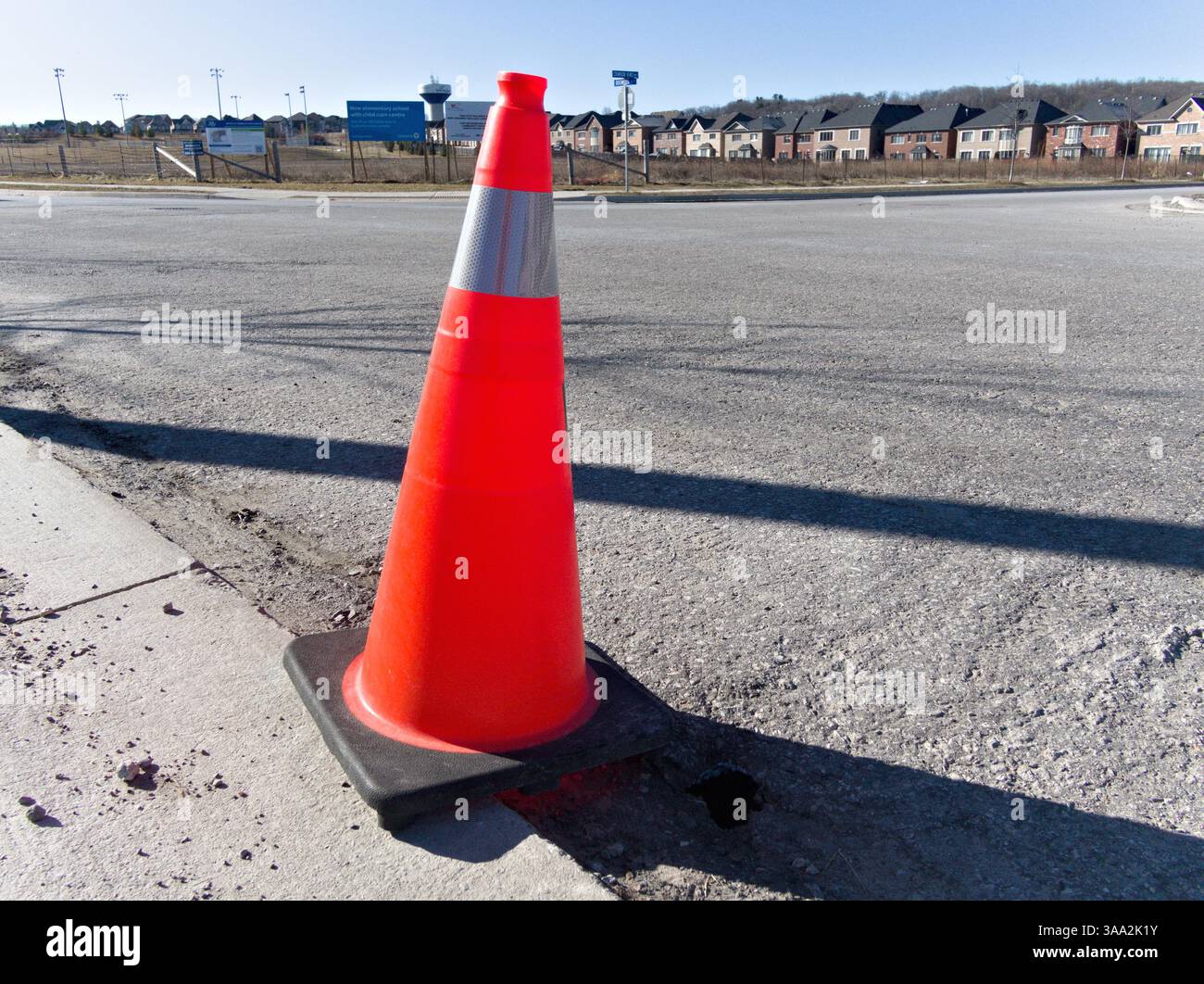 Un cono di traffico accattivante si trova stoicamente sullo sfondo di nuove case suburbane, segnando silenziosamente spazi di cautela e cambiamenti futuri Foto Stock