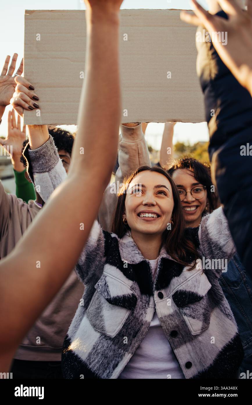 Un gruppo di persone allegre che partecipano a una protesta, con un cartello in bianco, e che dimostrano un sostegno e una difesa uniti per una causa comune. Foto Stock