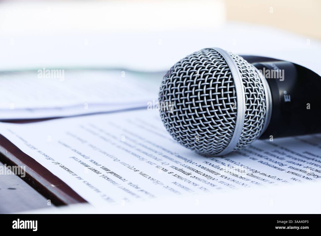 Il microfono si trova su pagine con testo su sfondo bianco. Primo piano. Messa a fuoco morbida. Concetto di registrazione audio di stampe, doppiaggio, ascolto. Ospitare una vigilia Foto Stock