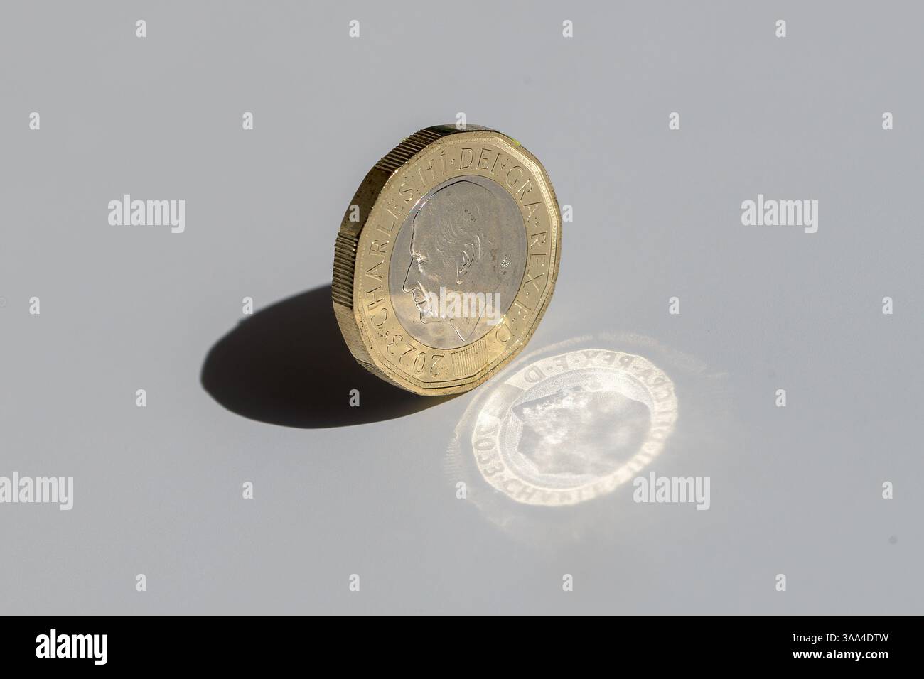 Una moneta inglese in libbre sul bordo con un'ombra e una riflessione luminosa audaci, che simboleggiano l'equilibrio, la ricchezza e la forza finanziaria nell'economia del Regno Unito Foto Stock