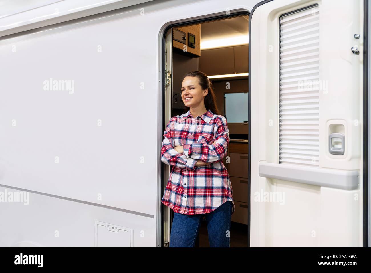 Proprietaria di camper sicura di sé all'ingresso del camper con braccia incrociate e sorridente Foto Stock